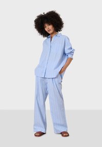 Blå och vit randig skjorta med knappar och lös passform, parat med matchande vida byxor. Slät, lättviktig tyg med fickdetaljer.