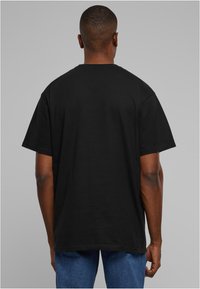 Tricou din bumbac negru, cu mâneci scurte, decolteu rotund și o croială lejeră, expus din spate. Textura pare netedă.
