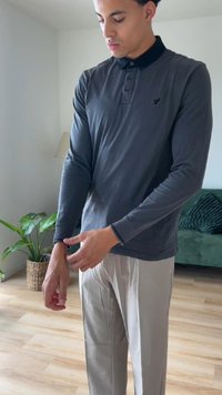 Tummanharmaa pitkähihainen polo-paita mustalla kauluksella ja logolla, yhdistettynä vaaleanbeigeihin housuihin neutraalissa taustassa.