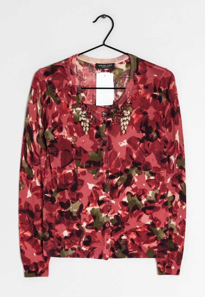 Cardigan fleuri avec un motif rose et vert, mettant en valeur un décolleté rond, des boutons sur le devant et des embellissements décoratifs sur la poitrine.