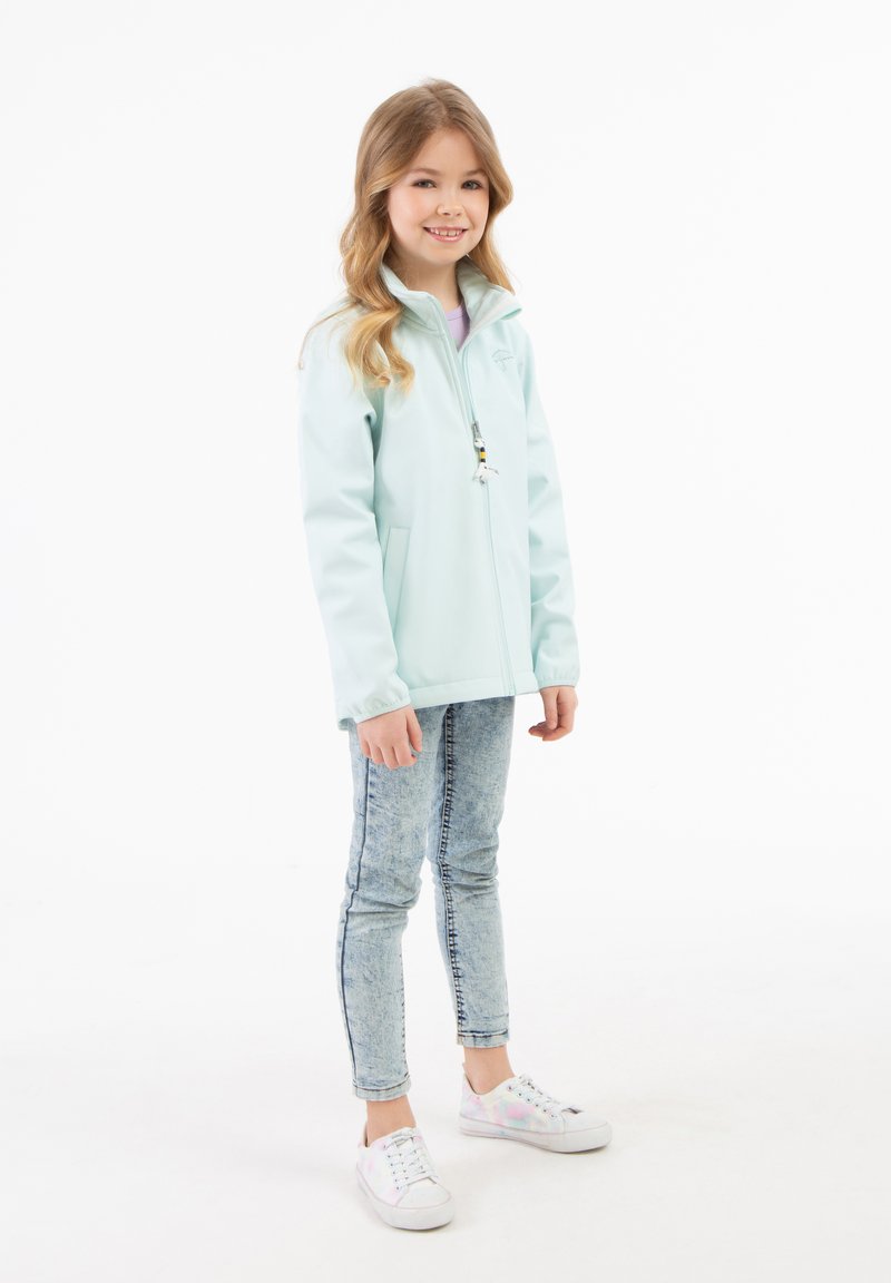 Giacca zip-up azzurra chiara con colletto alto, tasche frontali, abbinata a jeans blu sbiaditi e sneakers nei toni pastello. Tessuto liscio.