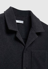 Chaqueta camisa negra de mezcla de lana con cuello, cierre de botones y un bolsillo en el pecho. Textura suave con un acabado sutil y elegante.