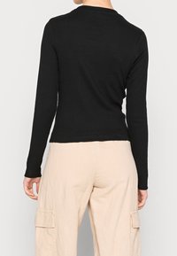 Schwarzes langärmliges, figurbetontes Oberteil mit gerippter Textur, Rundhalsausschnitt und cropped Saum, kombiniert mit beigen, locker sitzenden Cargo-Hosen.