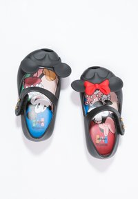 Chaussures en plastique noir avec des motifs de Mickey et Minnie Mouse, présentant des oreilles arrondies et un nœud rouge. Sangle de fermeture avec des accents dorés.