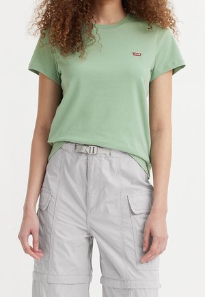 Woman wearing a light green Levi's t-shirt tucked into light gray cargo pants with a built-in belt, standing against a white background.