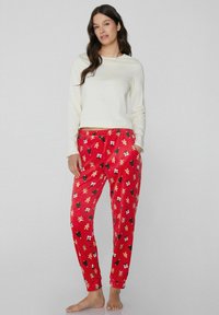 Czerwone spodnie od piżamy z świątecznymi wzorami choinek, prezentów i piernikowych ludzików. Połączone z kremową, długorękawową bluzką. Miękka faktura.