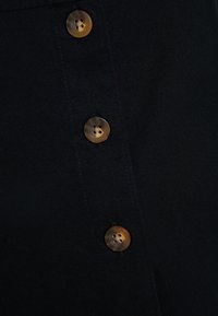 Svart tyg med en slät yta som har en rad av fyra rundade bruna knappar. Varje knapp har fyra hål och en subtil lyster.