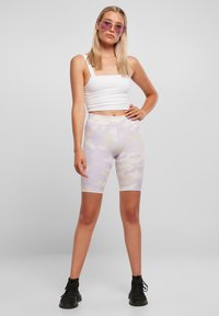 Cykelbukser i pastel lilla camouflage mønster, strækbart stof, midt på låret længde, kombineret med en tætsiddende hvid crop top og sorte sneakers.