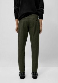 Vihreät puuvillahousut, joissa suora lahjemalli, takataskut ja sileä pinta. Yhdistetty mustaan neuleeseen ja mustiin kenkiin.