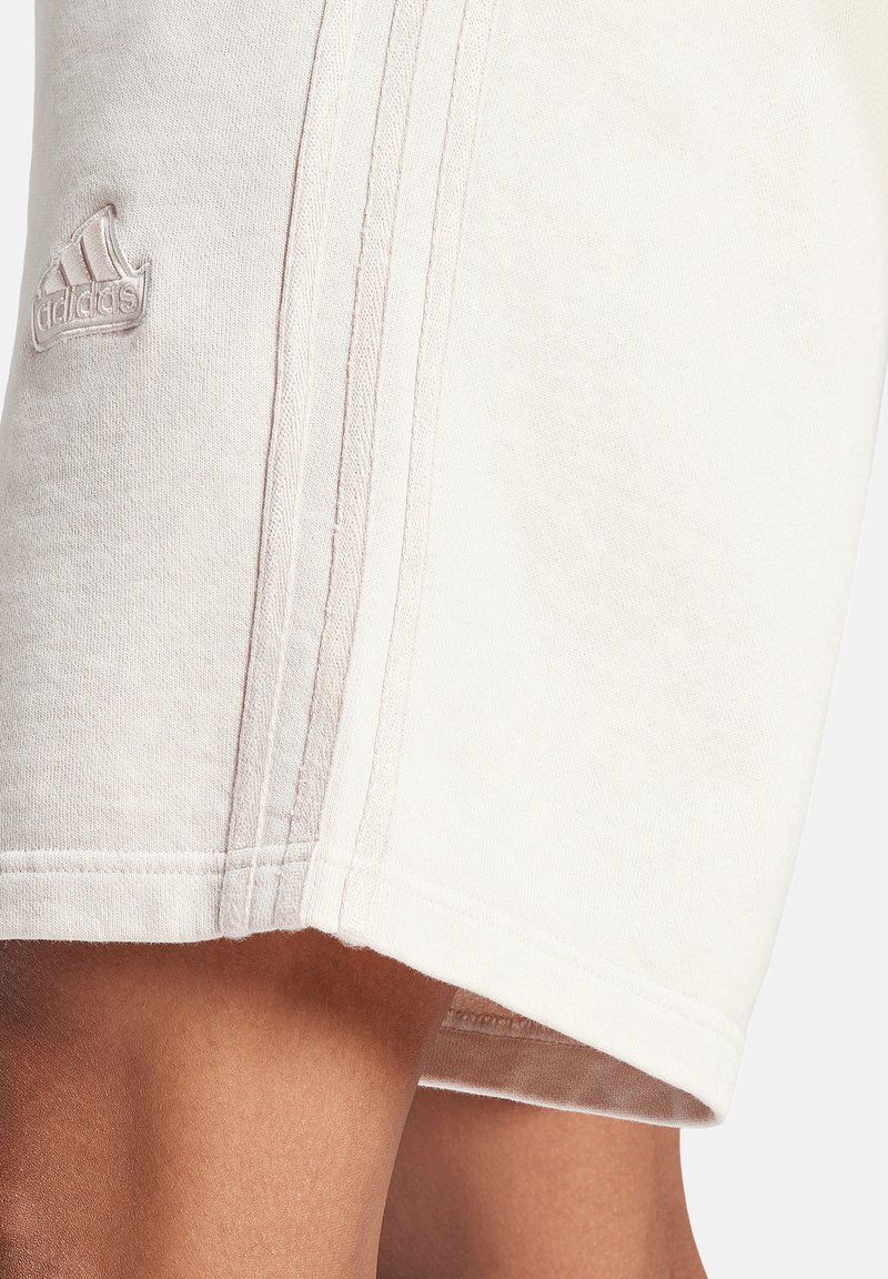Pantaloni corti beige con una texture morbida, caratterizzati da tre strisce verticali e un piccolo logo ricamato sulla cucitura laterale.
