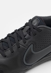 Czarne buty sportowe z cholewką skórzaną i z siateczki, okrągłym czubkiem, teksturowanymi detalami oraz tonowymi sznurówkami z wyraźnym logo po boku.