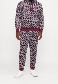 Patroon hoodie en joggers in donkerpaars met een wit en rood geometrisch ontwerp; heeft ribgebreide manchetten en onderzoom; gecombineerd met witte sneakers.