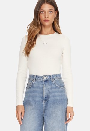 Maglietta bianca aderente a maniche lunghe con il logo "GUESS JEANS", abbinata a jeans di denim blu a vita alta, dalla vestibilità larga e con texture sbiadita.