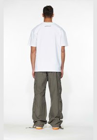 Bílý oversized T-shirt s logem na zádech, doplněný volnými olivovými cargo kalhotami s mnoha kapsami a šňůrkovými lemy.