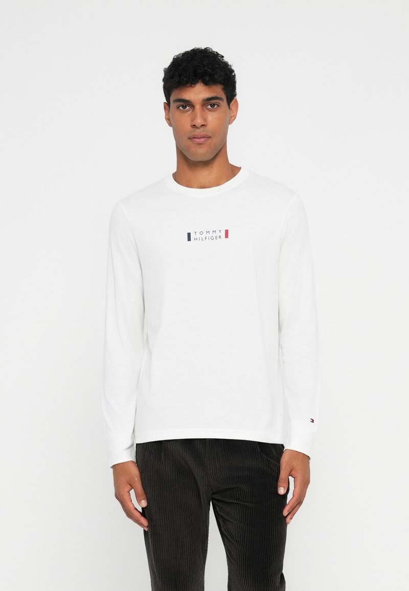 Bijela košulja dugih rukava s okruglim izrezom i malim logotipom "Tommy Hilfiger" u plavoj, crvenoj i crnoj boji na prsima. Pamuk.