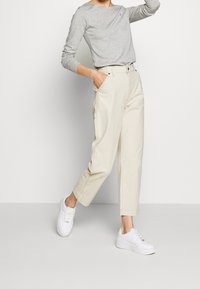 Šedá dlouhá rukávová košile s kulatým výstřihem, doplněná světle béžovými cargo kalhotami s bočními kapsami a bílými teniskami.