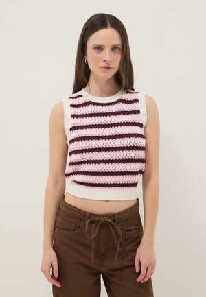 Young woman wearing a sleeveless cropped knit top with pink, brown, and white stripes and brown pants with a tied waist.