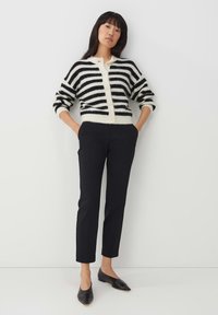 Zwart-wit gestreepte wollen cardigan met knopen, gecombineerd met zwarte tapered broek en zwarte ballerina's. Gladde textuur, ontspannen pasvorm.