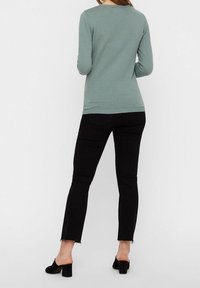 Långärmad, ljus turkos topp med texturerad tyg, rundad halsringning, kombinerad med svarta jeans med fransad fåll och åtsittande silhuett.