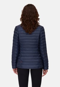 Marinblå puffjacka med horisontellt quiltat mönster, slät textur och en lätt rundad nederkant. Har en liten röd accent nertill.