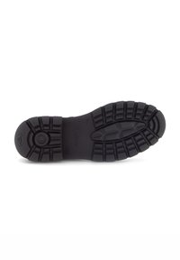 Suola di scarpa in gomma nera con un design testurizzato e a motivi, caratterizzato da scanalature per una migliore aderenza e un emblema circolare vicino al tallone.