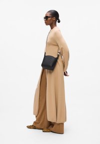Beige langermet kjole og vide bukser, med en teksturert svart crossbody-veske med preget logo og leopardmønstrede sko.