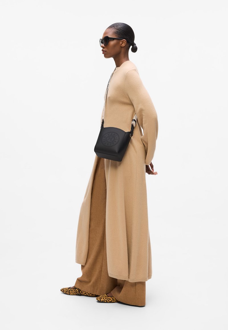Beige langermet kjole og vide bukser, med en teksturert svart crossbody-veske med preget logo og leopardmønstrede sko.