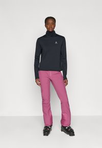 Langermige marineblauwe top met een hoge kraag en een textuurstof, gecombineerd met roze sneeuwbroeken. De laarzen zijn zwart met zilveren hardwareaccenten.