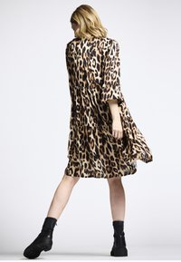 Kleid mit Leopardenmuster, das einen lockeren Schnitt, knielangen Design und Dreiviertelärmel aufweist, kombiniert mit schwarzen Knöchelstiefeln. Glatte Stofftextur.