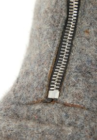 Gros plan d'une fermeture éclair métallique partiellement fermée sur un tissu en laine gris à surface texturée et duveteuse.