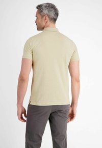 Lichtbeige polo shirt met korte mouwen en een kraag; gladde textuur; zijsplitten; gedragen met donkergrijze broek.