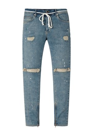 Jean slim bleu en denim avec taille à cordon, patchs usés sur les cuisses et les genoux, éclaboussures de peinture blanche et fermetures éclair aux chevilles.