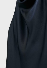 Tissu bleu marine foncé avec des plis doux et une texture lisse suspendu devant un arrière-plan gris clair.