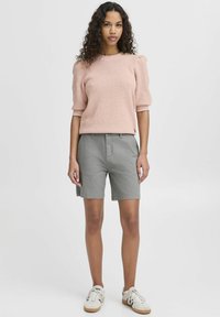 Suéter de punto texturizado de color rosa claro con mangas abullonadas, combinado con pantalones cortos de algodón gris claro y zapatillas blancas con acentos de color.