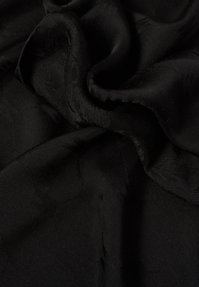 Tissu noir avec des motifs géométriques tissés subtils, délicatement plié pour montrer la texture et une légère brillance.