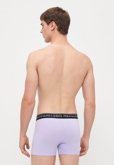 Ανοιχτό μωβ μποξεράκια με μαύρη ζώνη που φέρει λευκό κείμενο "POLO RALPH LAUREN", εμφανίζονται από πίσω σε γυμνό κορμό.