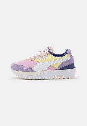 Zapatilla baja con malla rosa, paneles amarillos y beige, detalles en ante morado, franja blanca de Puma y suela blanca gruesa mirando hacia la derecha sobre fondo blanco.