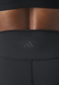 Černé sportovní legíny s hladkým, elastickým materiálem a přiléhavým pasem. Logo Adidas se nachází vzadu.