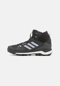 Zapato de senderismo negro con material Gore-Tex, con tres rayas gris claro, una parte superior texturizada y una entresuela blanca. Suela robusta para tracción.