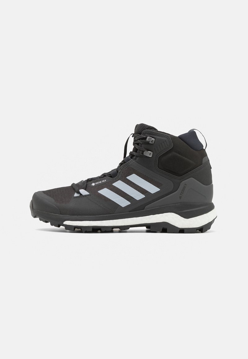 Zapato de senderismo negro con material Gore-Tex, con tres rayas gris claro, una parte superior texturizada y una entresuela blanca. Suela robusta para tracción.