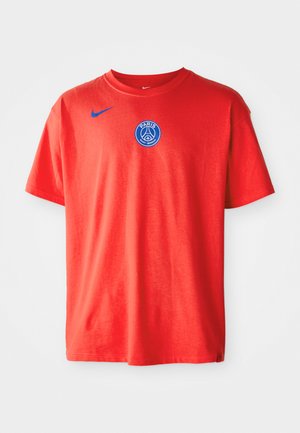 Red cotton t-shirt featuring a blue Nike logo on the left shoulder and a blue Paris Saint-Germain badge at center chest. Short sleeves.