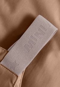 Hnedá látka s svetloružovým elastickým pásom, na ktorom sú embosované texty a vzor hviezd, s detailmi šitia a hladkým povrchom.