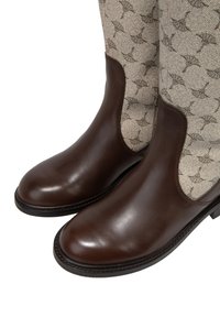 Stivali ankle in pelle marrone con una finitura liscia e lati elastici, abbinati a un tessuto crema con un sottile motivo a foglie.