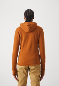 Orange, åtsittande hoodie med känguruficka och justerbar huva, parat med beige cargobyxor. Slät textur, minimalt varumärkesdetalj.