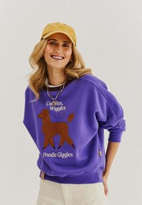 Fialová mikina s grafickým motivem hnědého pudla a textem "Cuddles, Wiggles, Poodle Giggles". Směs bavlny, volný střih, žebrované manžety.