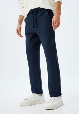 Marineblaue Sweatpants ausTextil mit elastischem Bund und Kordelzug. Kombiniert mit weißen Sneakers und präsentiert einen lässigen Schnitt.