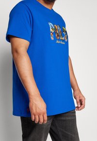 Blå bomullströja med en iögonfallande, färgglad "Polo" grafik med detaljerade motiv, kompletterad med en liten broderad logotyp vid fållen.