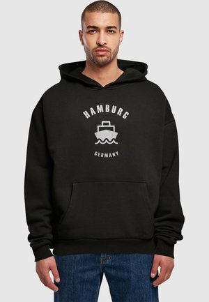 Black hoodie with a kangaroo pocket, featuring a white graphic print of a ship and the text "HAMBURG GERMANY" in a circular design.