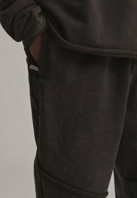 Ciemnoszary materiał na sweatshirt o teksturowanym wykończeniu, z kieszenią i kontrastowym przeszyciem. Miły w dotyku, casualowy krój z luźnym fasonem.