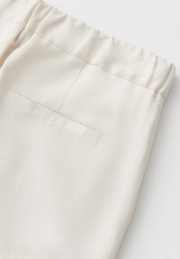 Cream-colored pants with elastic waistband and single back welt pocket, shown from the back upper section.